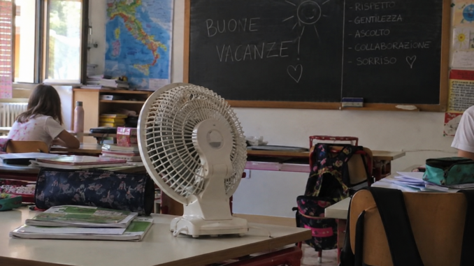 Ventilatore su un banco in una classe scolastica con lavagna e materiale didattico.