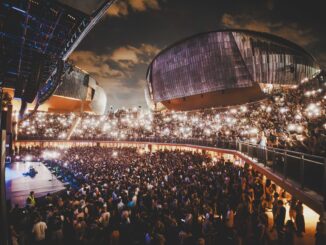 Veduta notturna dell'Auditorium Parco della Musica con moltissime persone sedute e in piedi durante un concerto.