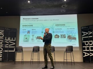 Persona che parla in un auditorium davanti a una presentazione proiettata con il logo Alpha Innovation e contenuti relativi all'innovazione di Fujifilm.