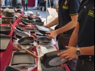 Agenti della Guardia di Finanza controllano borse e altri prodotti in un mercato all'aperto sotto un tendone.