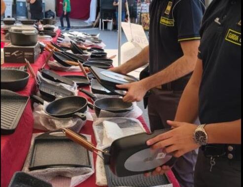 Agenti della Guardia di Finanza controllano borse e altri prodotti in un mercato all'aperto sotto un tendone.
